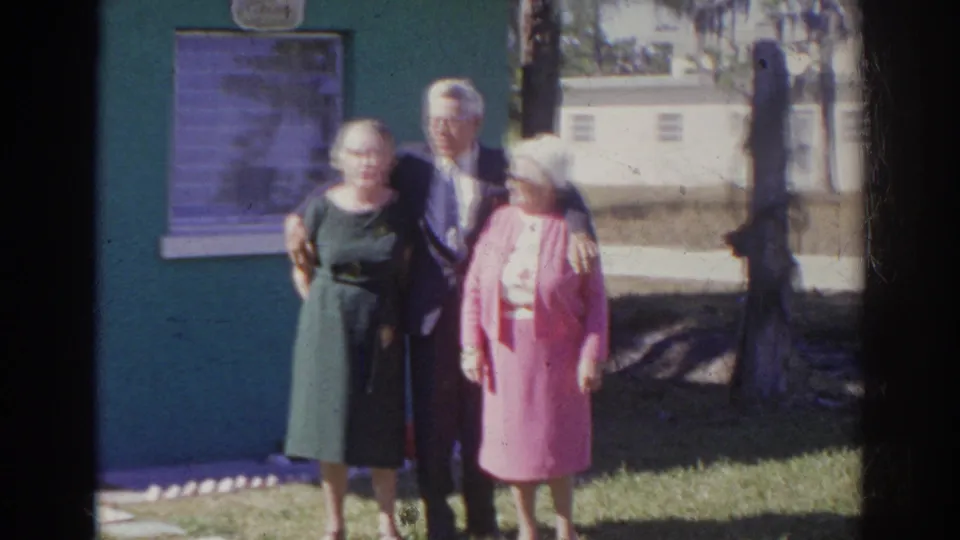 The posed trio remains outside the green building, with the man between two women in 1966 Norfolk home-movie footage.