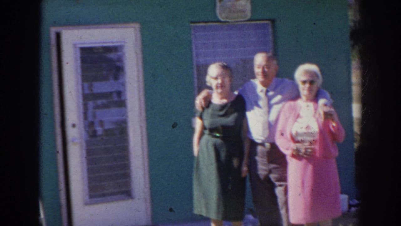 The group continues posing outside the Norfolk house, with the man placing his arms around two women near a white door and window.