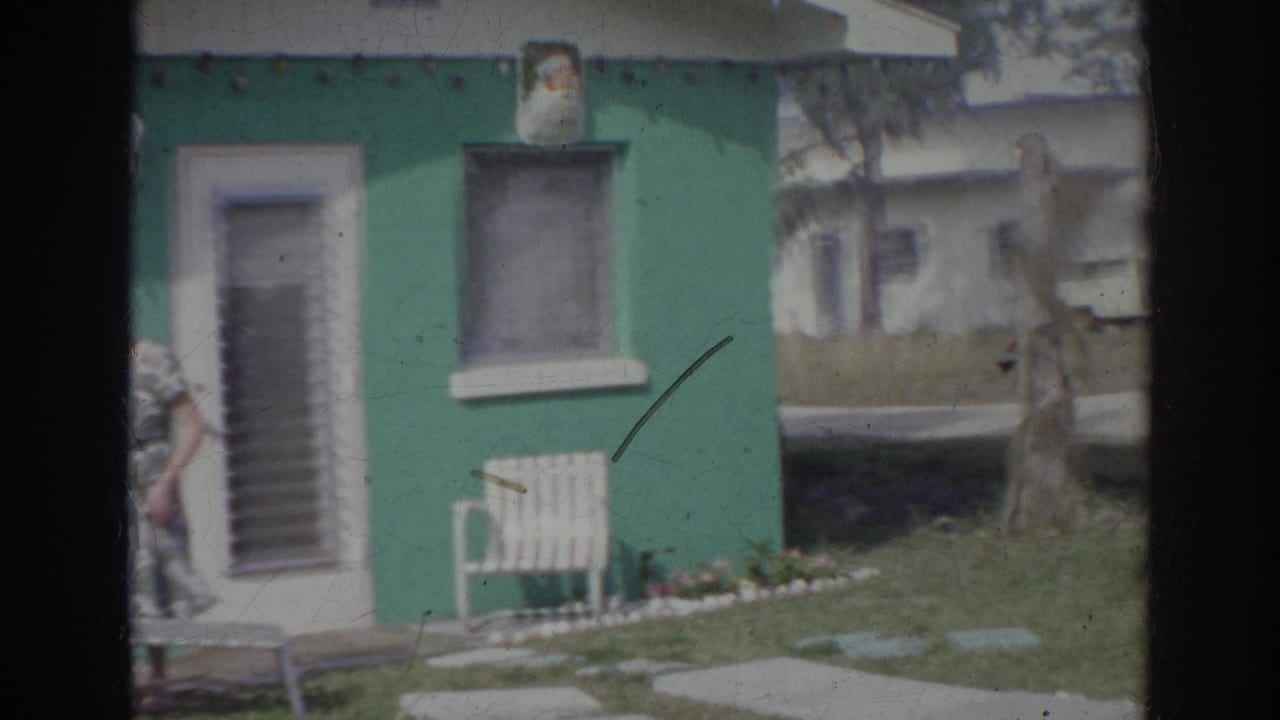 Teal house exterior with white door, window, lawn chair, and a woman partly visible at the left edge.