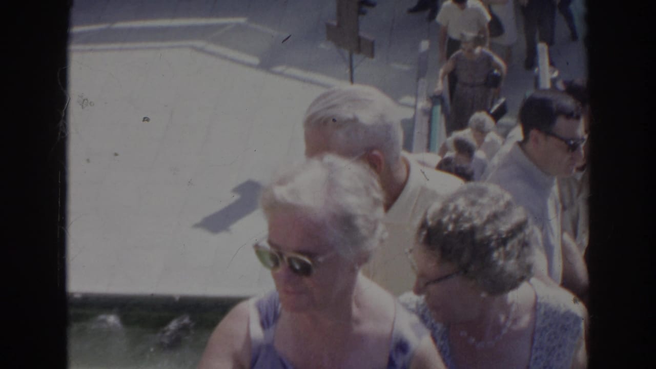 A crowded 1966 home-movie view shows older adults ascending concrete stairs, with sunglasses and light summer clothing visible.