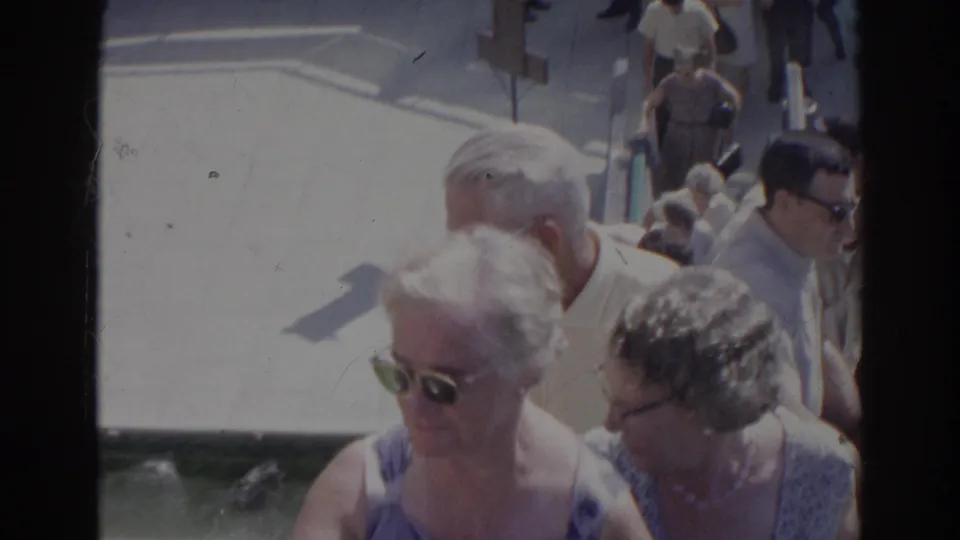 A crowded 1966 home-movie view shows older adults ascending concrete stairs, with sunglasses and light summer clothing visible.