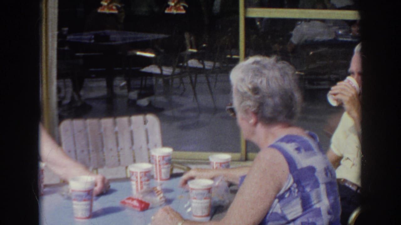Older diners seated at a light blue table with paper cups near cafe windows.