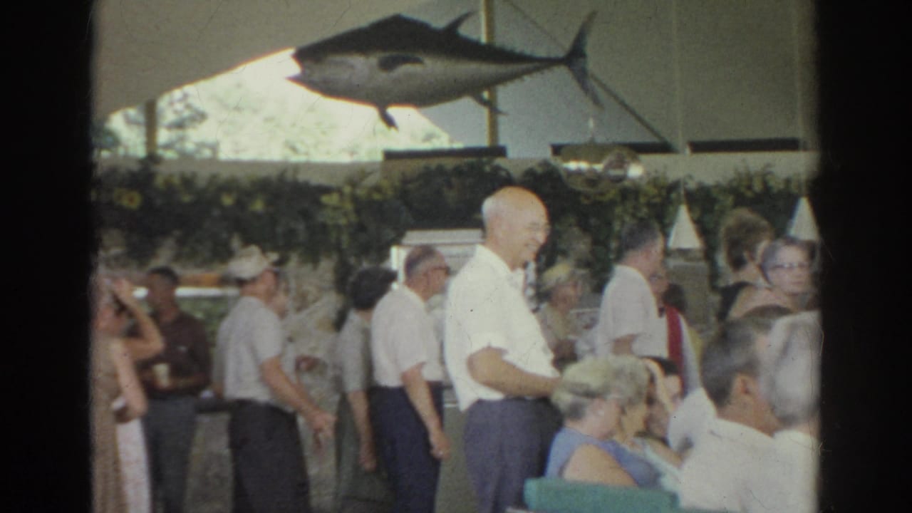 Older adults mingle and sit beneath a large fish decoration in a crowded indoor venue.