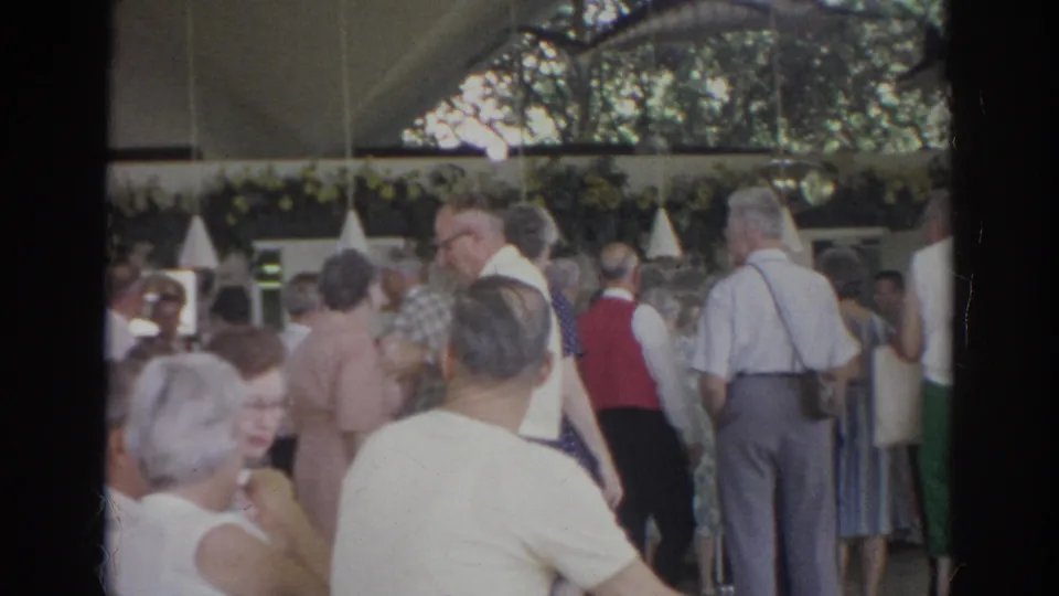 1966 Norfolk mixer scene with older adults in dress shirts and dresses gathered inside a decorated restaurant or club room.