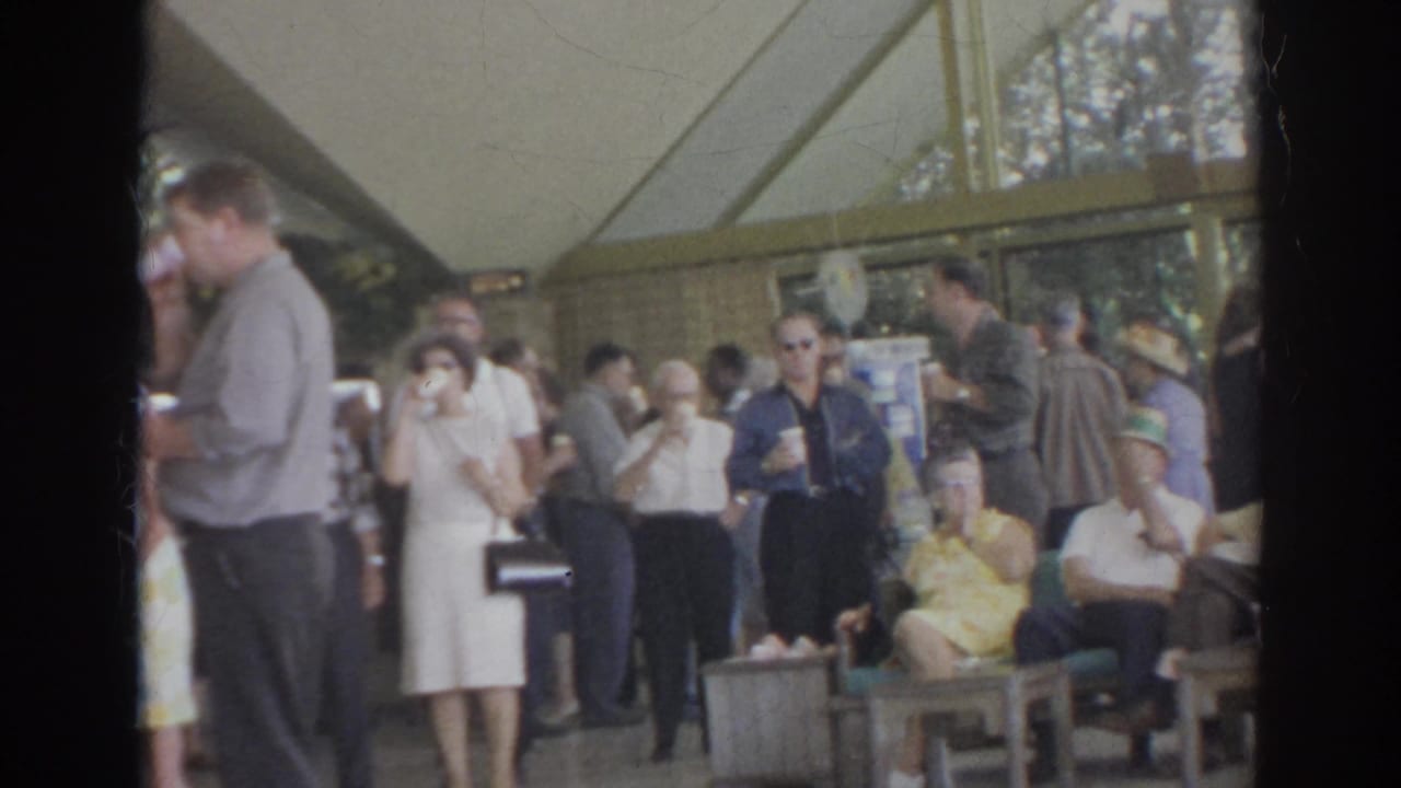 1966 Norfolk social scene with adults seated and standing under a pavilion canopy, several holding drinks in a candid home-movie view.