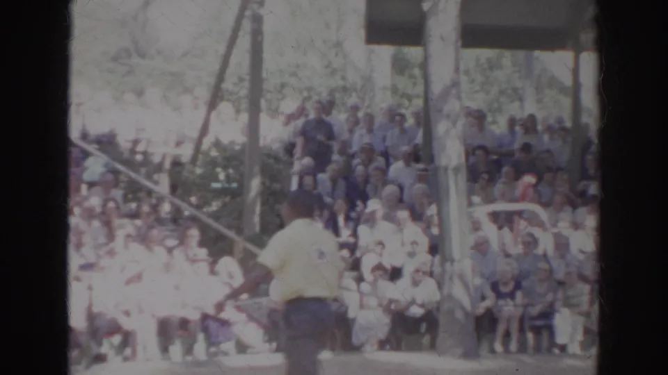 Light-shirted trainer stands with his back to the camera before a large Norfolk bird-show audience in 1966 footage.