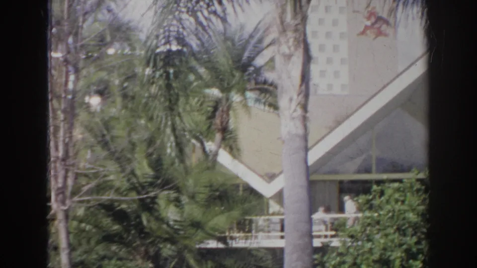 1966 Norfolk home-movie frame of palms in front of a pale modern exterior with an angular roof and porch area.