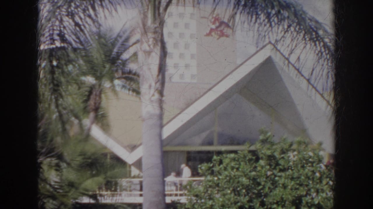 1966 Norfolk exterior view with palms, angular architecture, greenery, and a distant person on the porch.