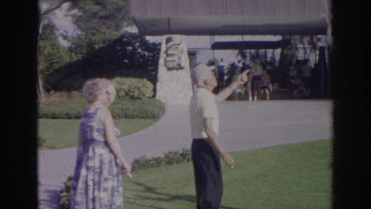 Adult man points near a stone monument while a woman stands on a paved path.