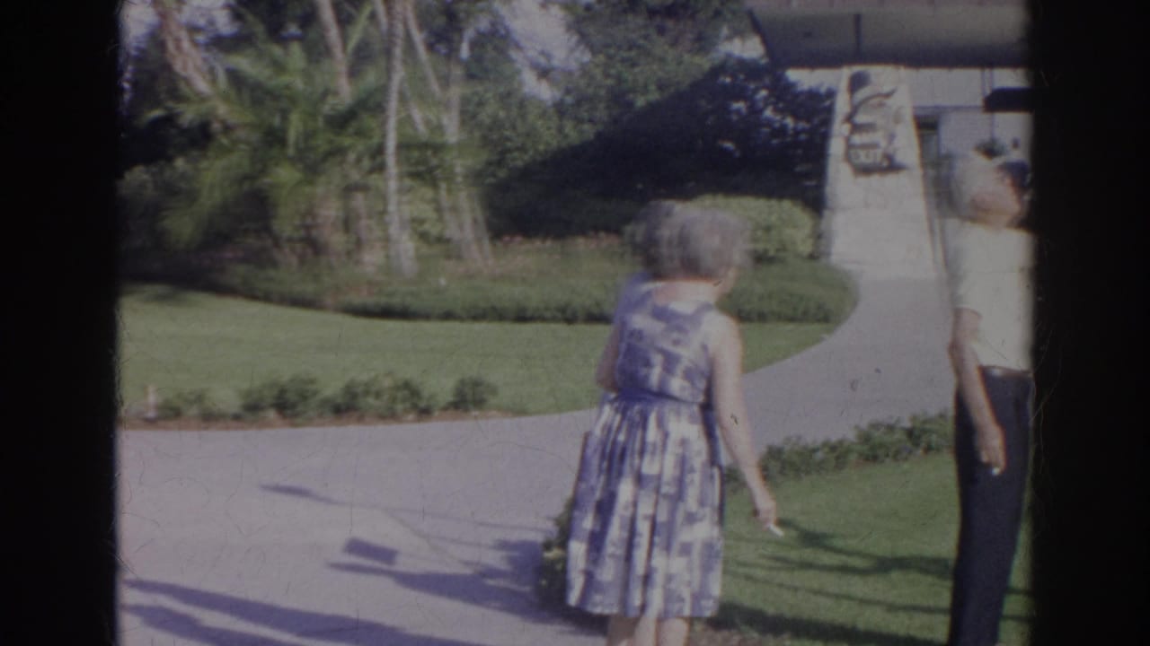 1966 Norfolk visitor footage showing a woman walking past manicured landscaping and a stone monument at a tourist attraction.