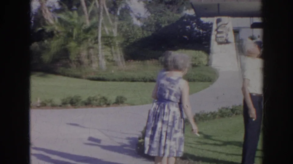 1966 Norfolk visitor footage showing a woman walking past manicured landscaping and a stone monument at a tourist attraction.