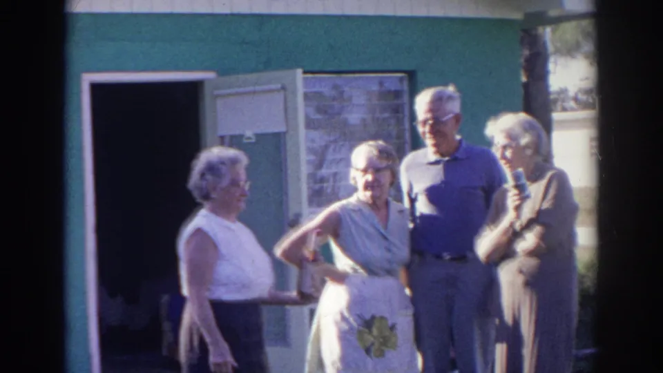 Four adults converse outside a green building in Norfolk, Virginia 1966, captured with soft handheld 8mm framing.