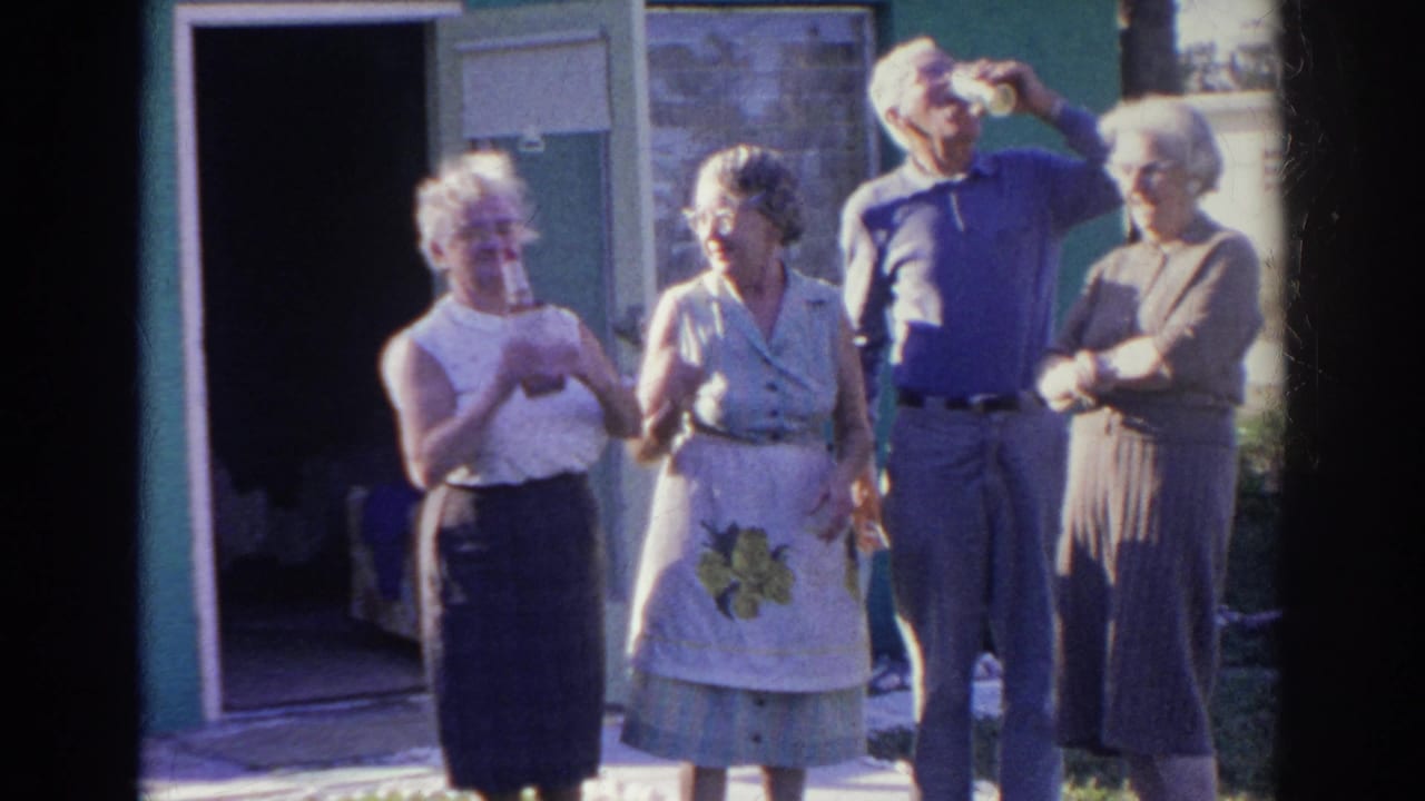 Four older adults stand near an open doorway outside the green house.