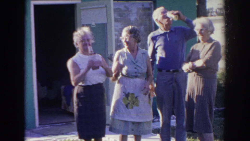 Older adults in Norfolk, Virginia, appear outside an open doorway, holding cups and standing together in bright daylight.