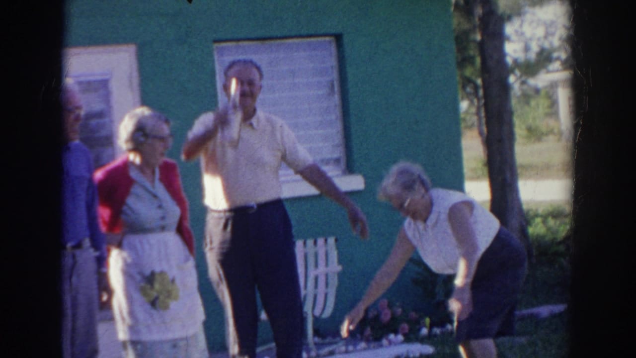 Older adults stand outside a green house while one man raises a bottle.