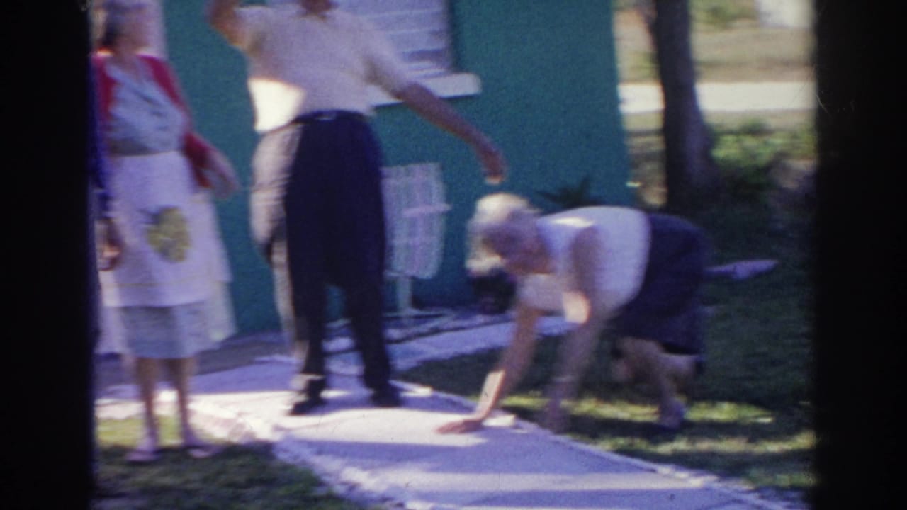 Adults stand near a walkway while one person bends down on the grass.