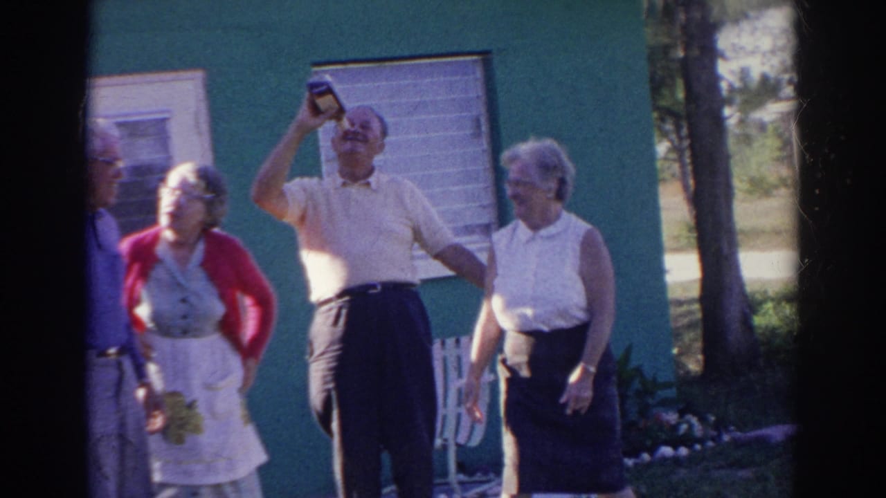Older adults stand outside a green house while a man raises a bottle to his mouth.