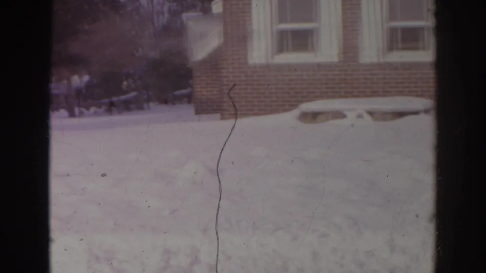 A snowy residential yard appears in the home-movie sequence, facing a brick house with shuttered windows and low window wells.