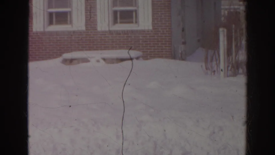 1966 Norfolk home-movie frame showing snow piled across a residential yard before a brick house with white-trimmed windows.