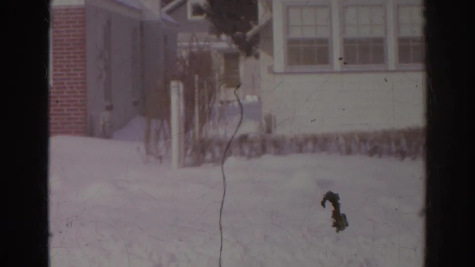 1966 Norfolk home-movie view of a pale-sided house, windows, bare shrubs, and deep snow across the front yard.