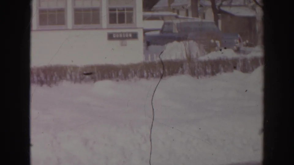 1966 Norfolk 8mm still showing a dark parked car beside a snow-covered hedge and the white DOBSON building.