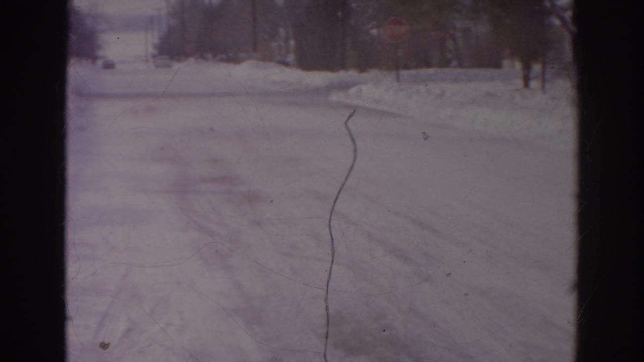 Snow-covered residential street seen through dark film borders.