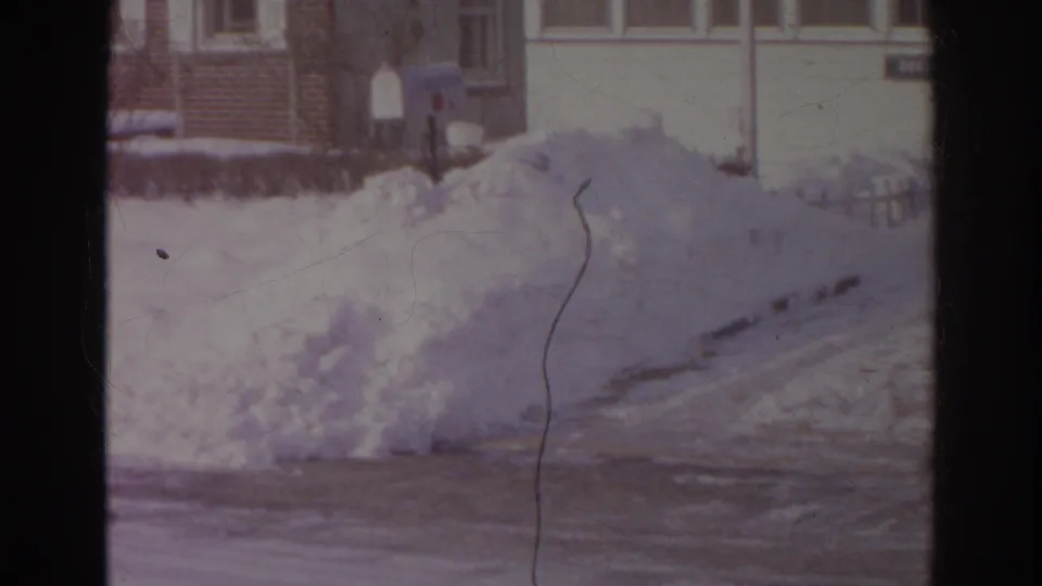 Norfolk home-movie still from 1966 showing a roadside snow pile, house fronts, mailboxes, and a dark vertical film divider.