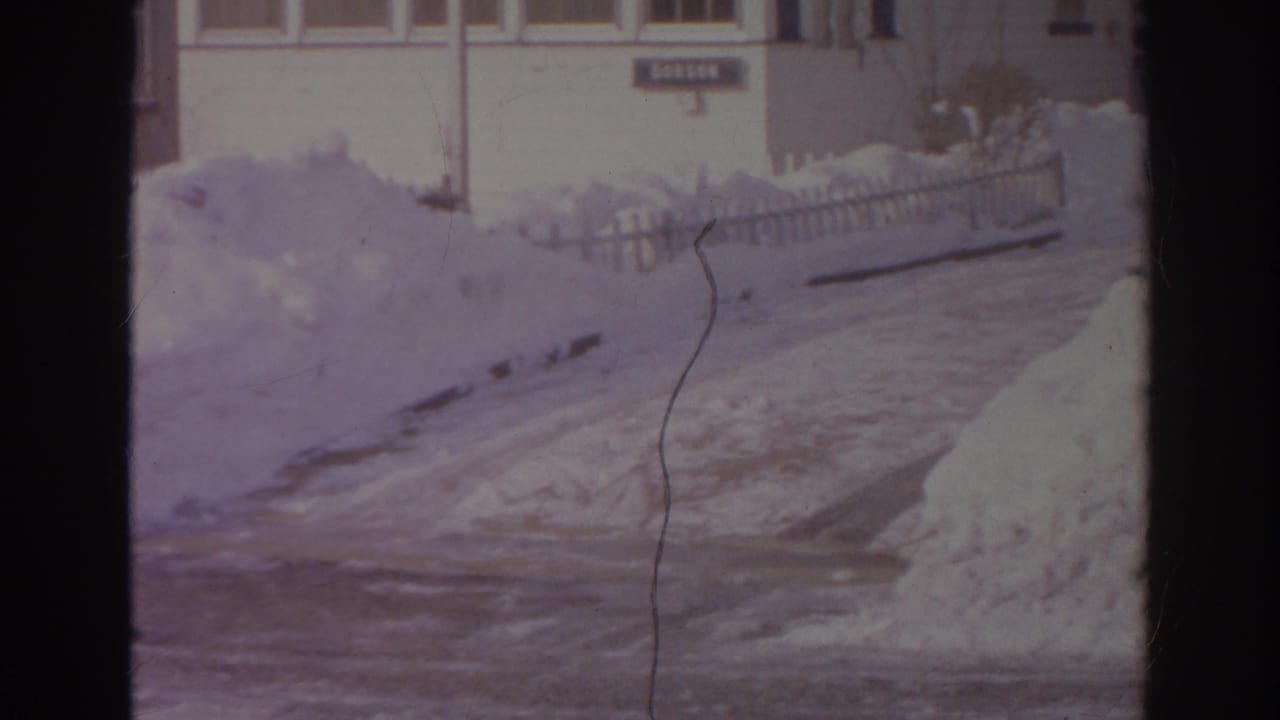Snowbanks beside a residential street with picket fencing and house fronts in the background.