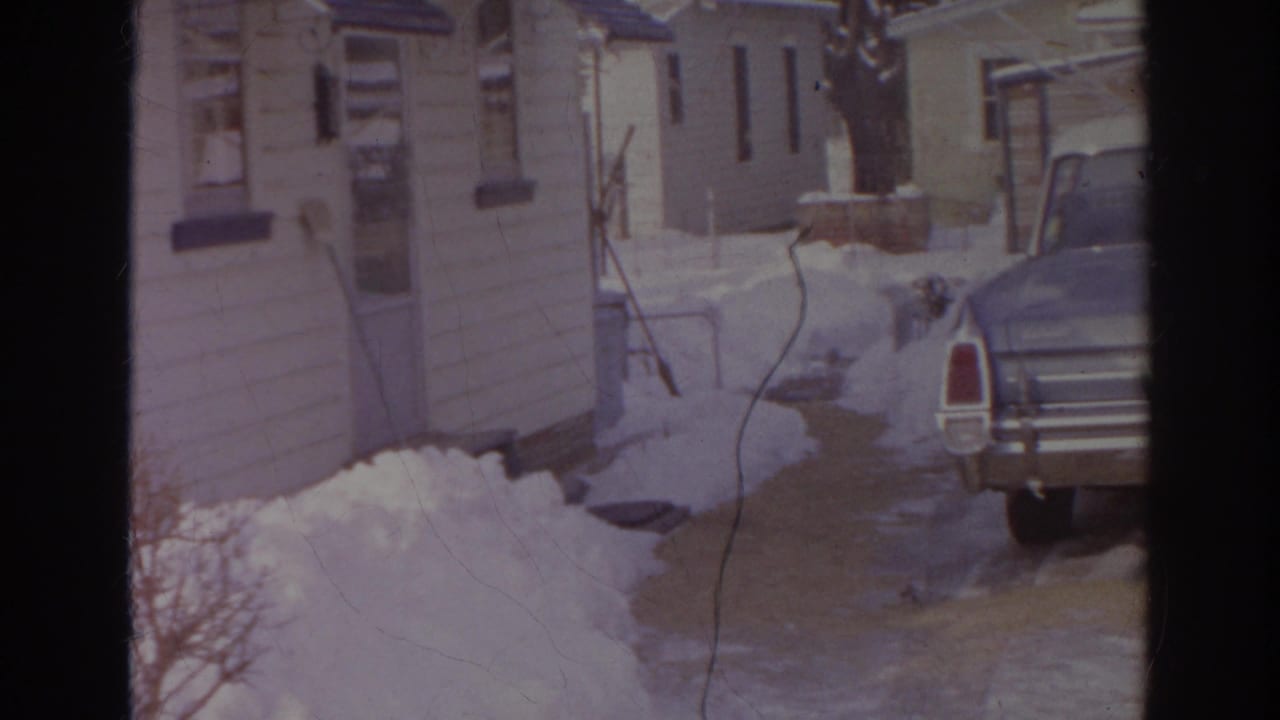 Blue sedan parked beside snowbanks near tan residential buildings.