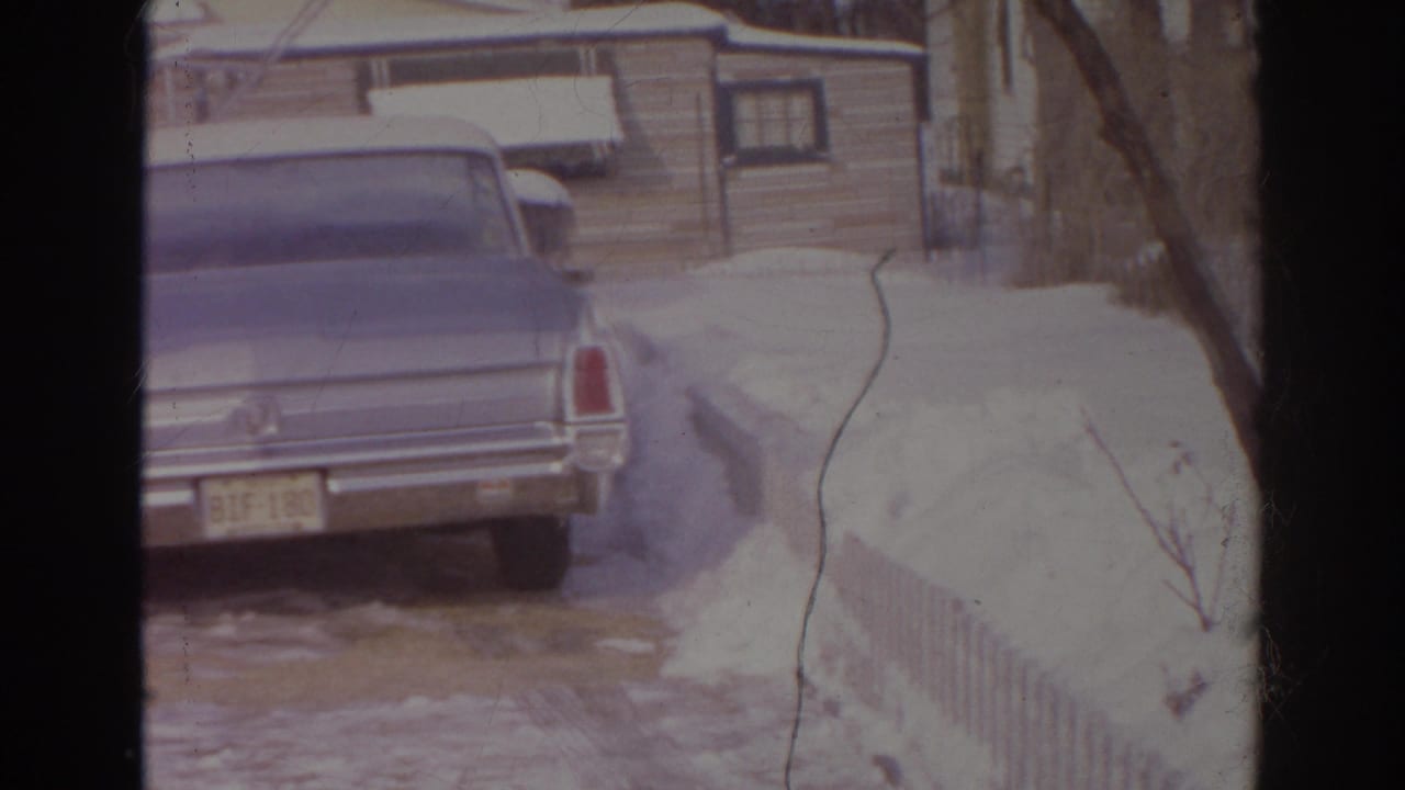 Blue sedan in a Norfolk residential driveway, with snow piled along a low fence and small houses in the background.