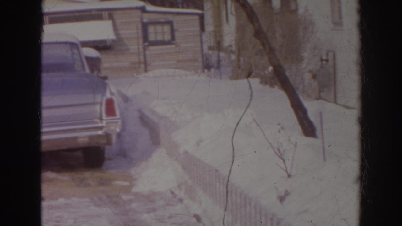 1966 Norfolk home-movie frame showing a blue car parked near a snowy residential driveway and house exterior.