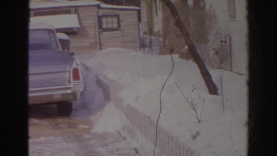 1966 Norfolk home-movie frame showing a blue car parked near a snowy residential driveway and house exterior.
