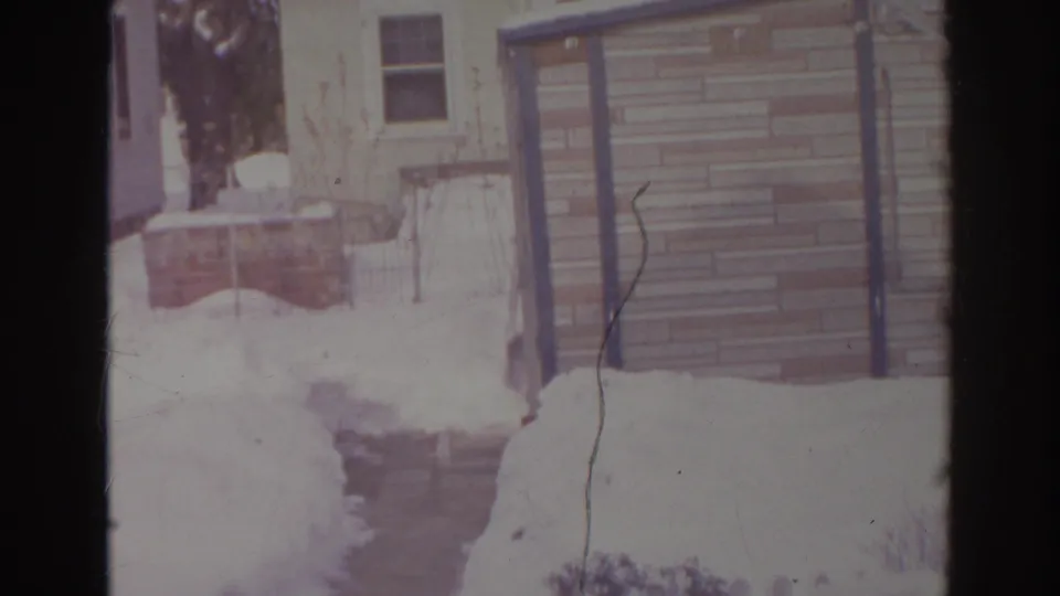 1966 Norfolk backyard after snow, with a narrow cleared path, small shed, brickwork, and house siding visible.