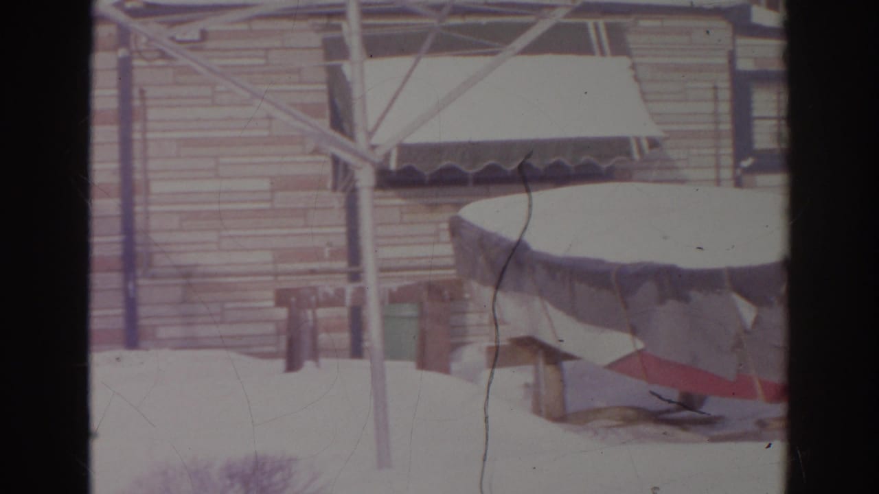 A covered backyard area in 1966 Norfolk appears surrounded by deep snow, with posts, siding, and a low roofline visible.