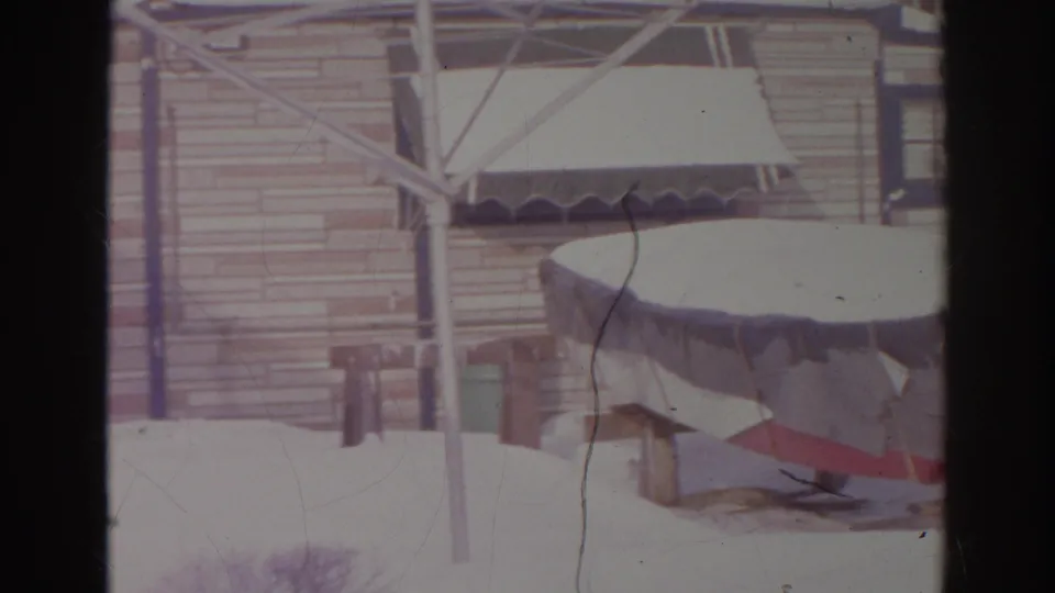 A covered backyard area in 1966 Norfolk appears surrounded by deep snow, with posts, siding, and a low roofline visible.