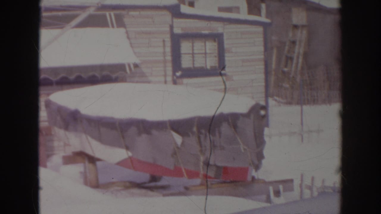Snow rests on a covered boat and trailer in a Norfolk, Virginia backyard, with house siding and windows behind it.