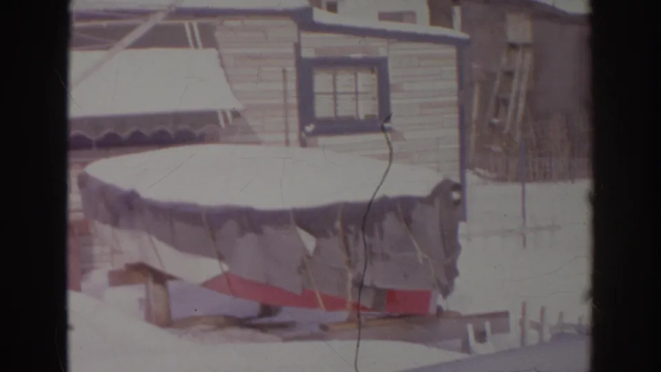 Snow rests on a covered boat and trailer in a Norfolk, Virginia backyard, with house siding and windows behind it.