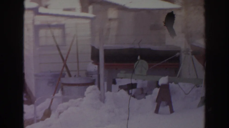 A 1966 home-movie frame shows a snowy Norfolk backyard with clothesline poles, yard items, and part of the covered boat.