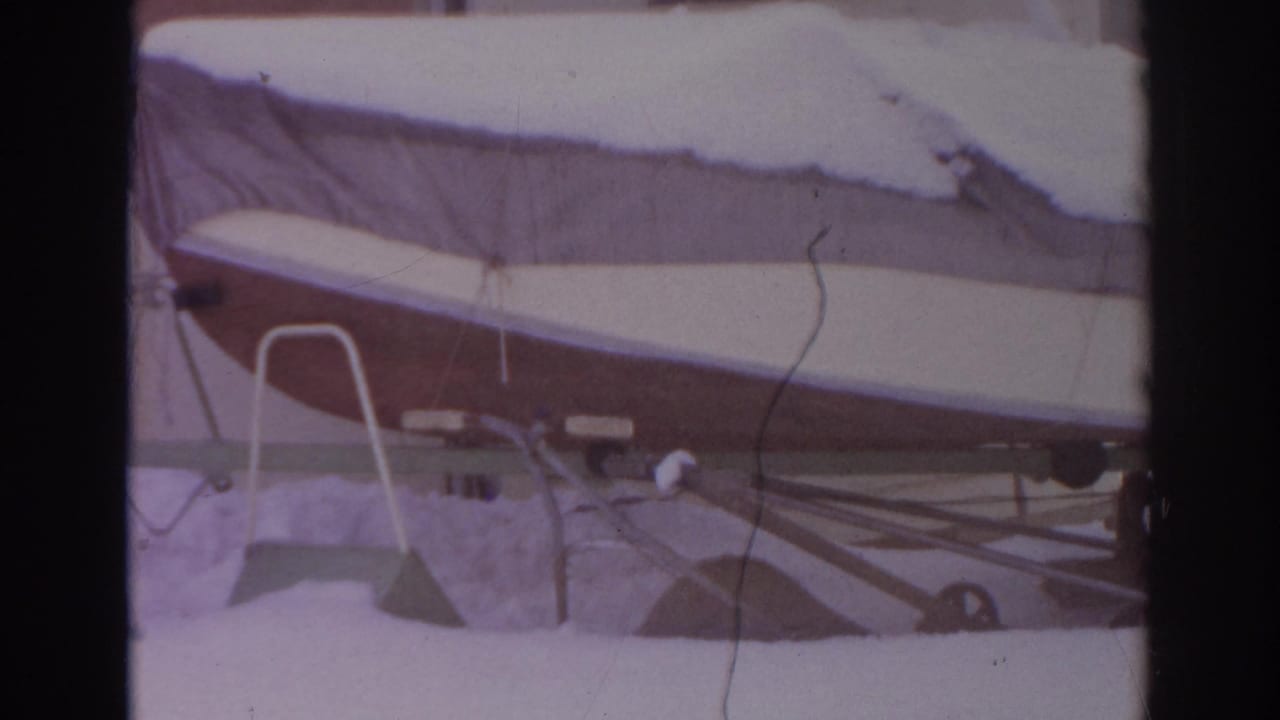 1966 Norfolk, Virginia frame of a snow-blanketed covered boat on a trailer in a residential yard, with siding in the background.