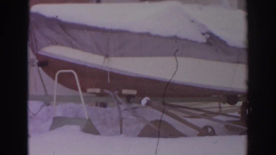 1966 Norfolk, Virginia frame of a snow-blanketed covered boat on a trailer in a residential yard, with siding in the background.
