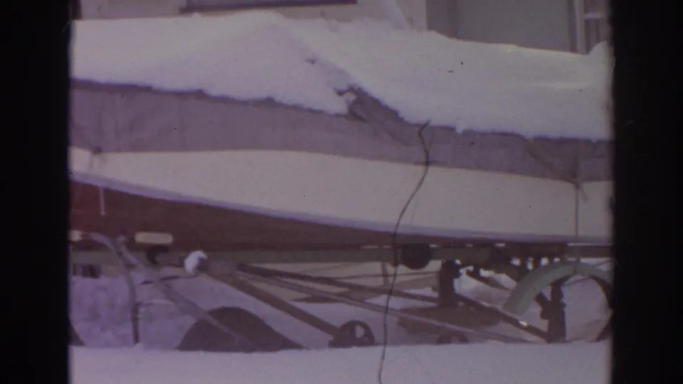 1966 Norfolk, Virginia home-movie frame showing the side of a covered boat with snow piled on top and trailer parts below.