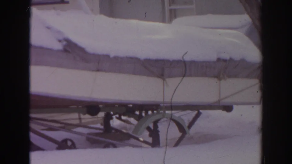 1966 Norfolk, Virginia frame showing a covered boat in winter storage, with trailer wheel hardware and residential siding behind it.