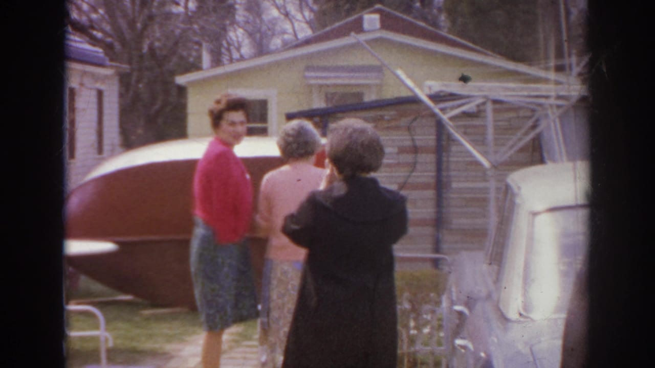 Adults stand in a residential yard near a light-colored car and an overturned boat.