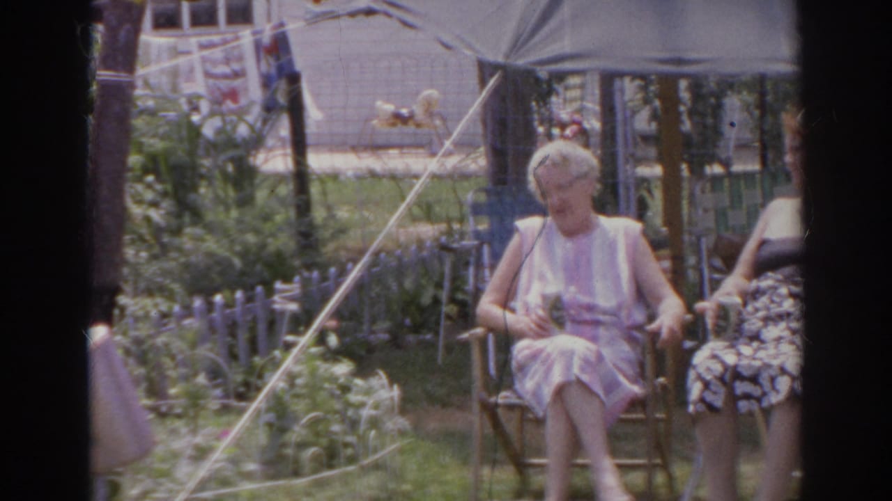 Two older women sit in folding chairs under a large backyard umbrella.