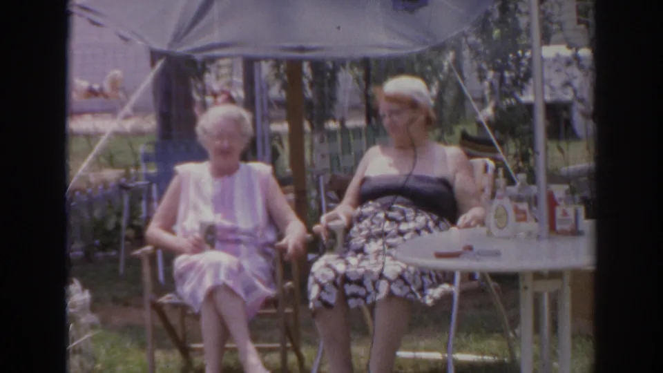 Two older women sit under a patio umbrella beside a small table in Norfolk, Virginia home-movie footage from 1966.