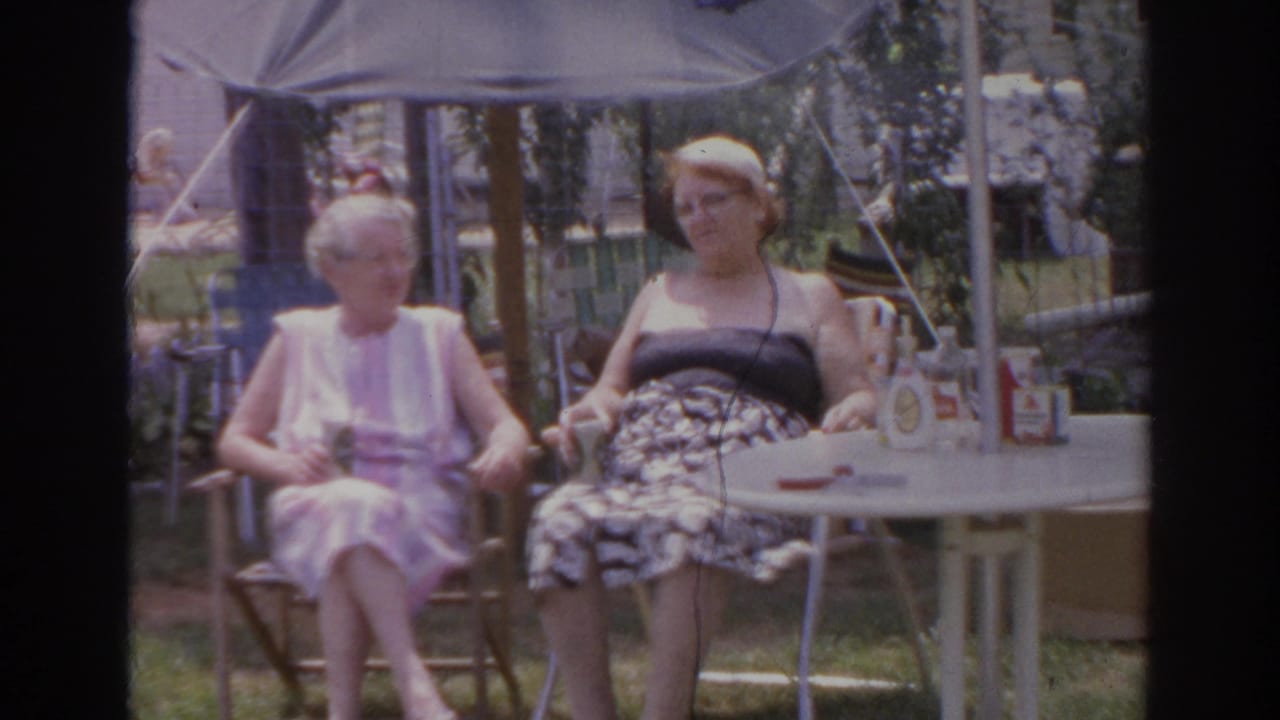 Two women seated outdoors under a patio umbrella at a small table.
