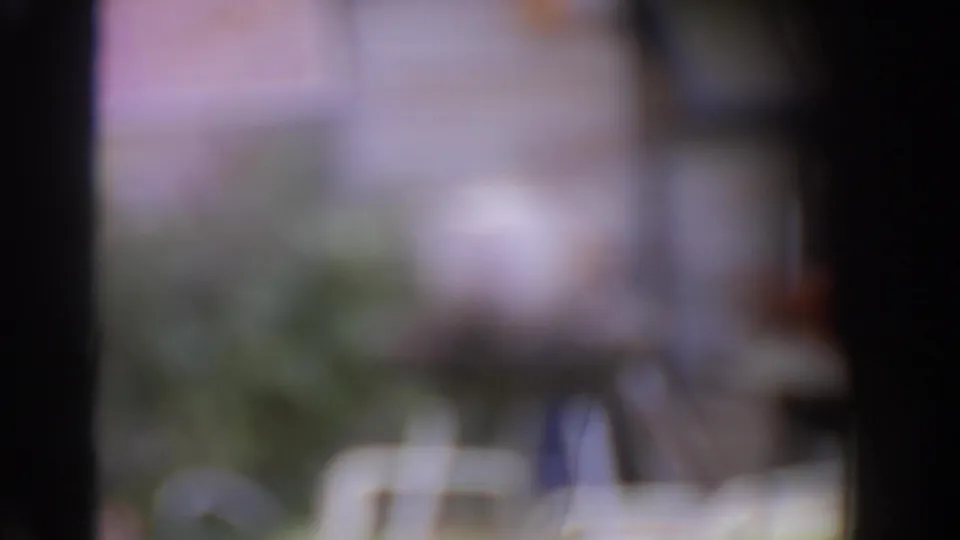 Soft out-of-focus 8mm frame from the Norfolk patio scene, with plants, grill area, and foreground obstruction blurred.