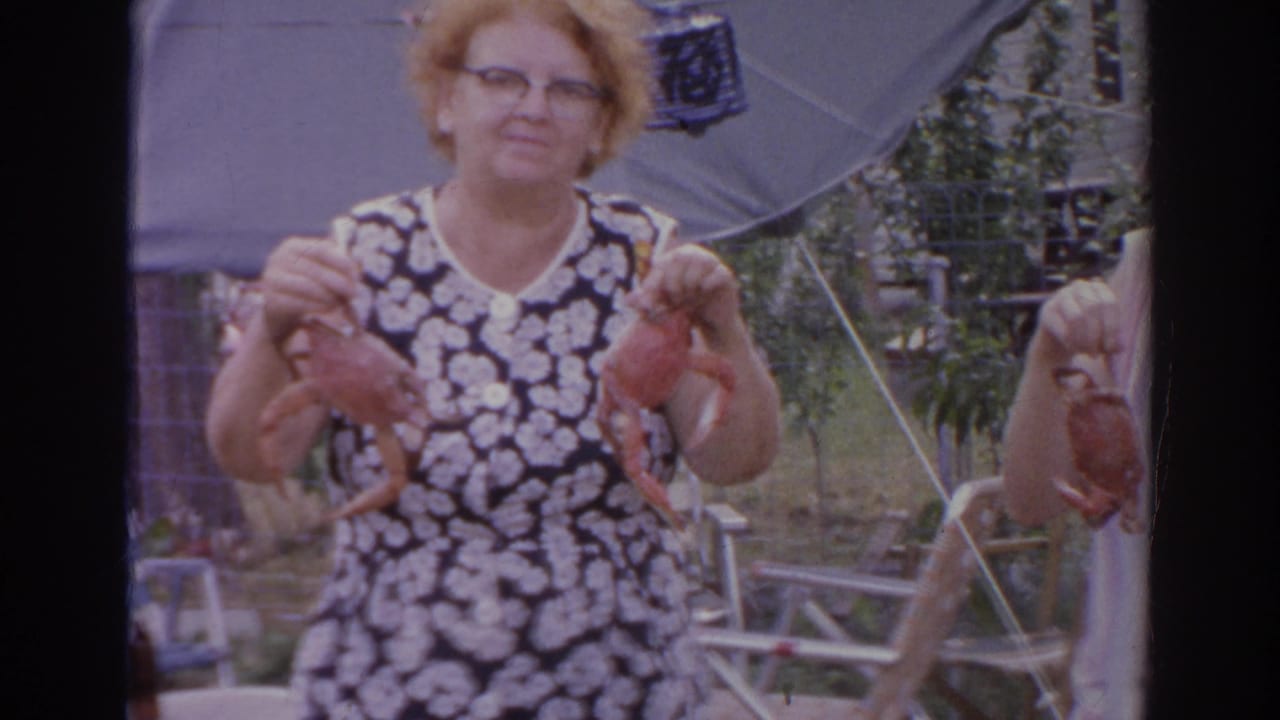 Woman in a floral dress holds two crabs in a backyard.