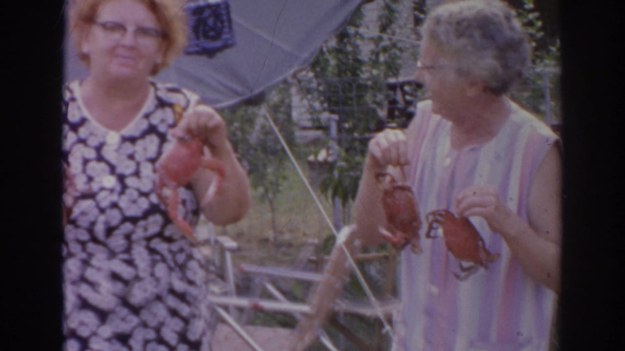 Two women stand outdoors holding crabs near lawn chairs.