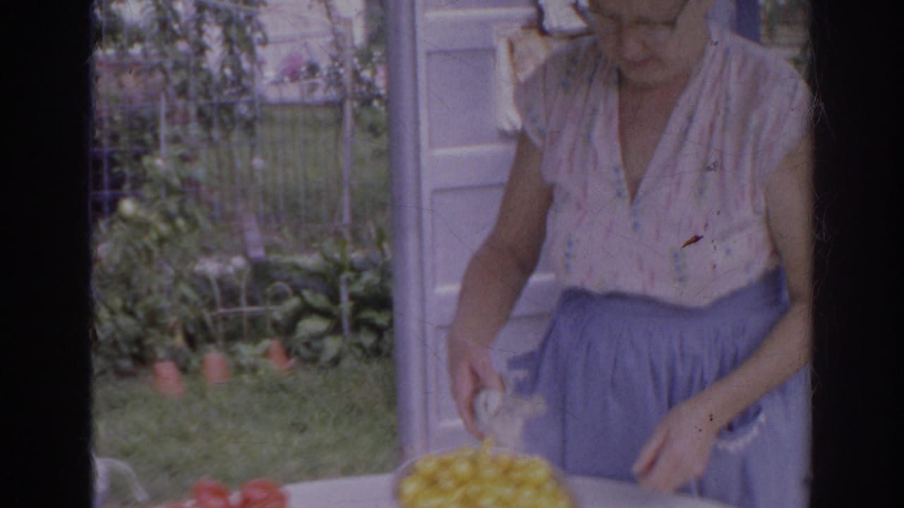 Woman wearing glasses handles a bowl of yellow tomatoes at an outdoor table.
